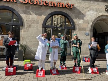 Sechs Personen in verschiedenen Berufsoutfits stehen auf roten Boxen mit der Aufschrift 'equal pay day' in der Fußgängerzone.