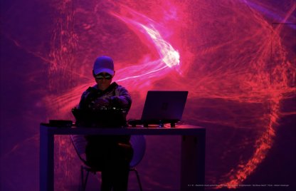 Digity am DJ-Pult. Rote- und Magentafarbene Lichteffekte wabern durch den Raum.