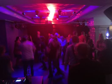 Menschen tanzen in der Kellerbühne mit roter und blauer Beleuchtung und einer Discokugel an der Decke
