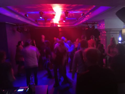 Menschen tanzen in der Kellerbühne mit roter und blauer Beleuchtung und einer Discokugel an der Decke