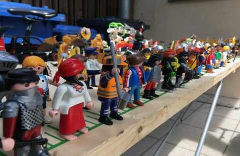 Reihe von Playmobil-Figuren in verschiedenen Kostümen und Farben auf einem Holzbrett