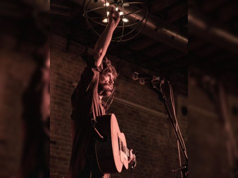 Eamonn McGrath mit Gitarre hebt einen Arm vor Mikrofon