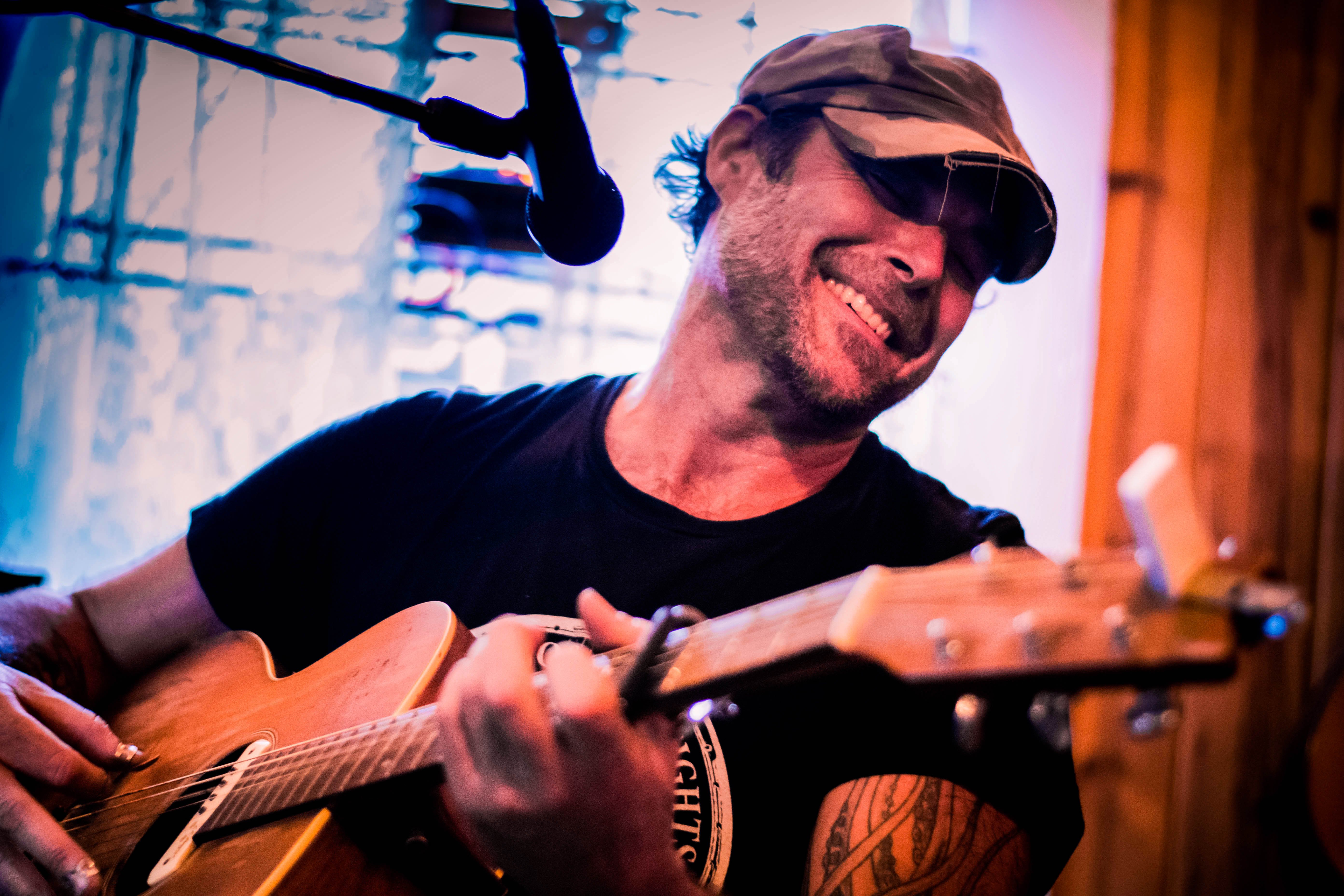 Ein Mann mit Cap und Akustikgitarre hinter einem Mikrofon