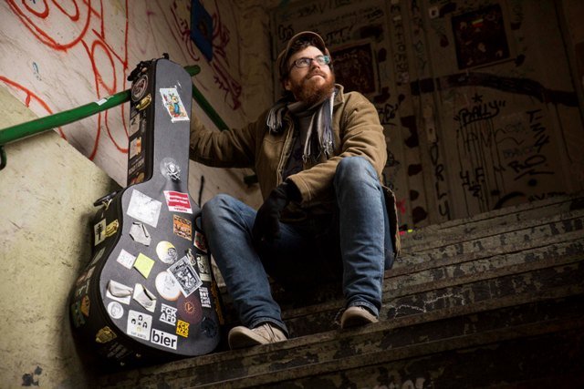 Ein Mann mit einem Gitarrenkoffer sitzt auf einer Treppe