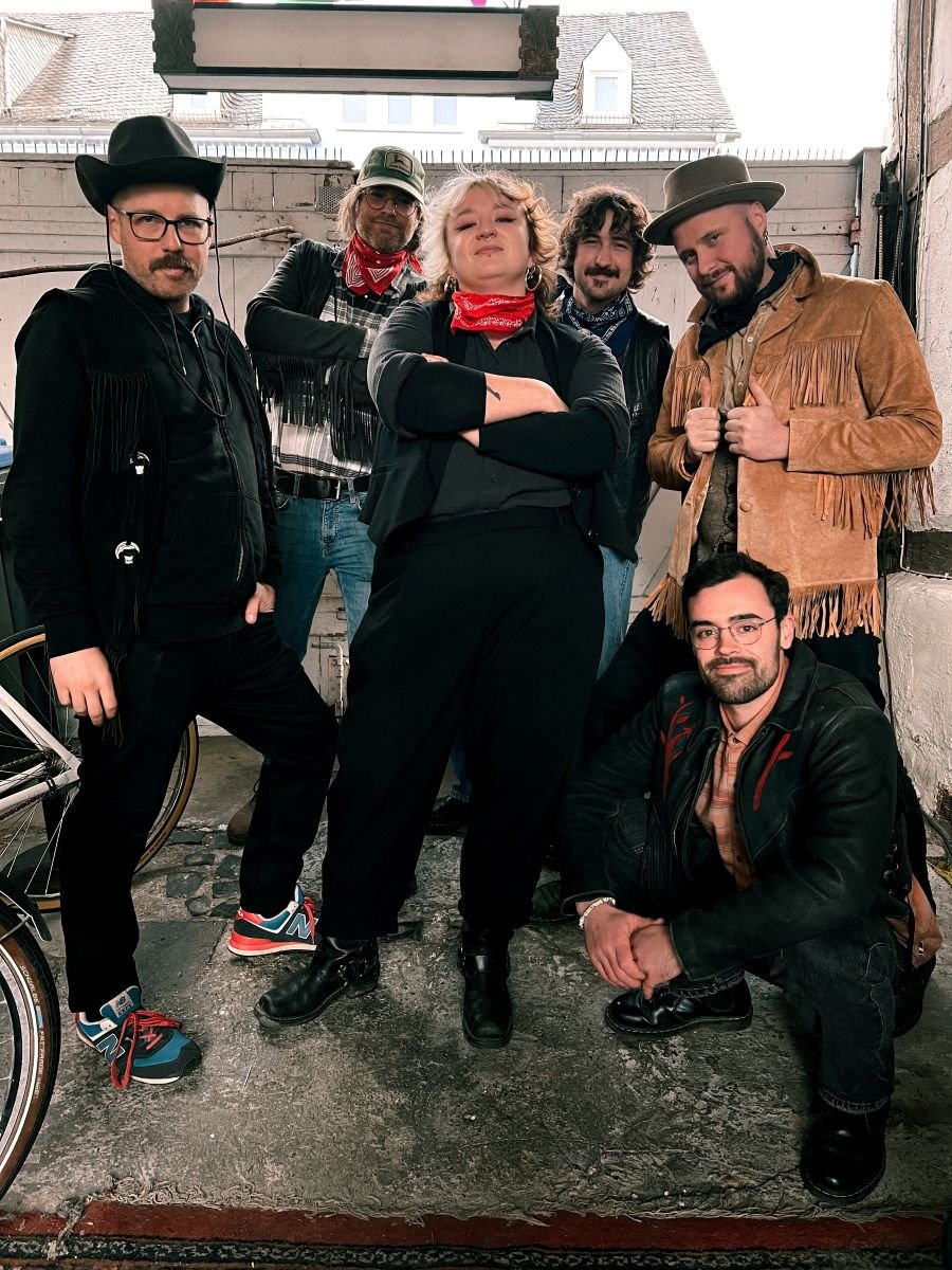 5 Männer und eine Frau stehen in Westernkleidung in einer Lagerhalle