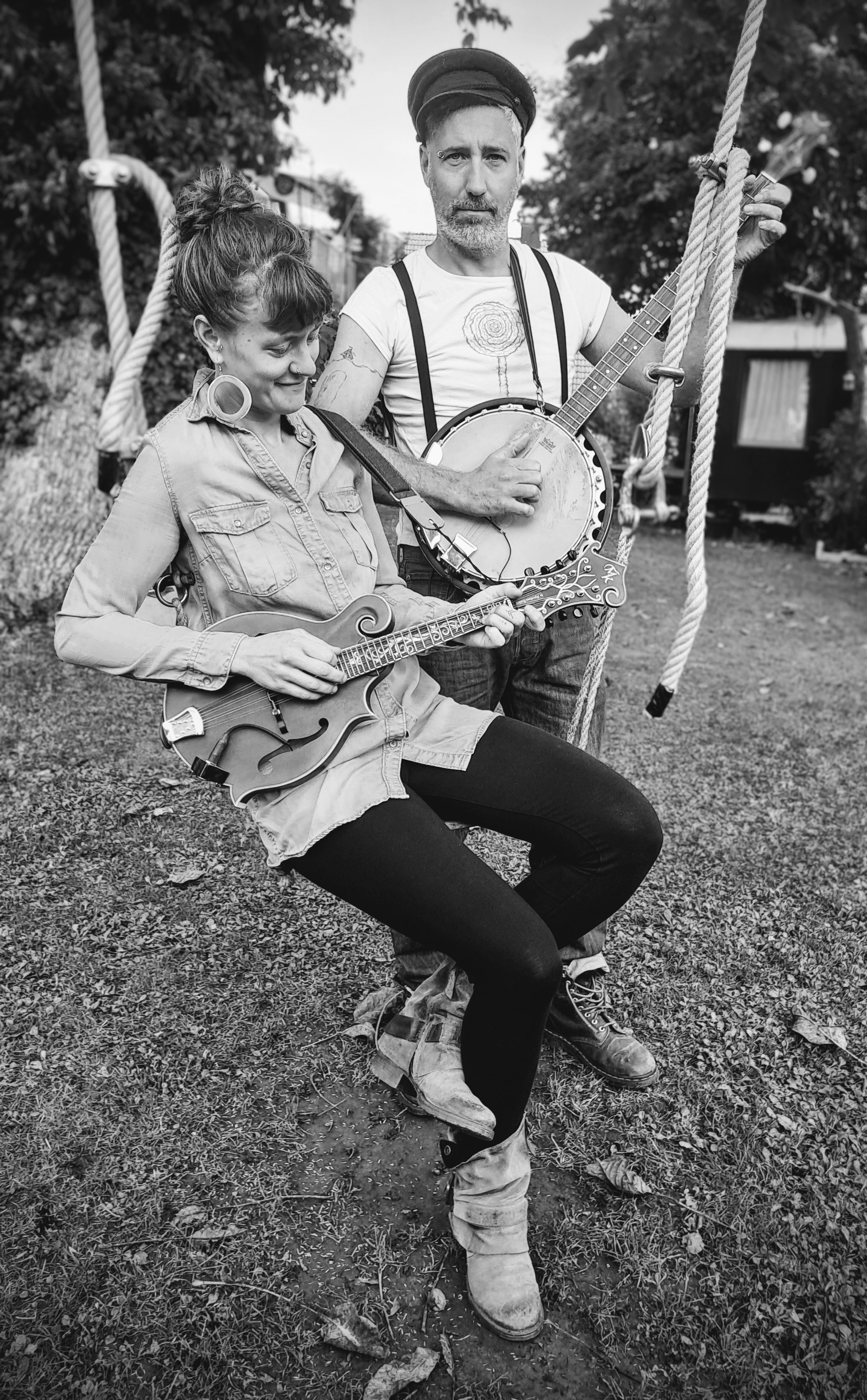 Ein Mann und eine Frau auf einer Schaukel. Beide mit Musikinstrumenten. Schwarz-weiß Foto