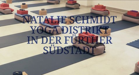 Mehrere Yogamatten mit zusammengefalteten Decken und kleinen Holzkästen in einem hellen Raum mit hohen Fenstern