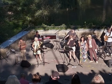 Band mit mehreren Musikern und Sängerinnen auf der Freilichtbühne mit Instrumenten und Mikrofonen