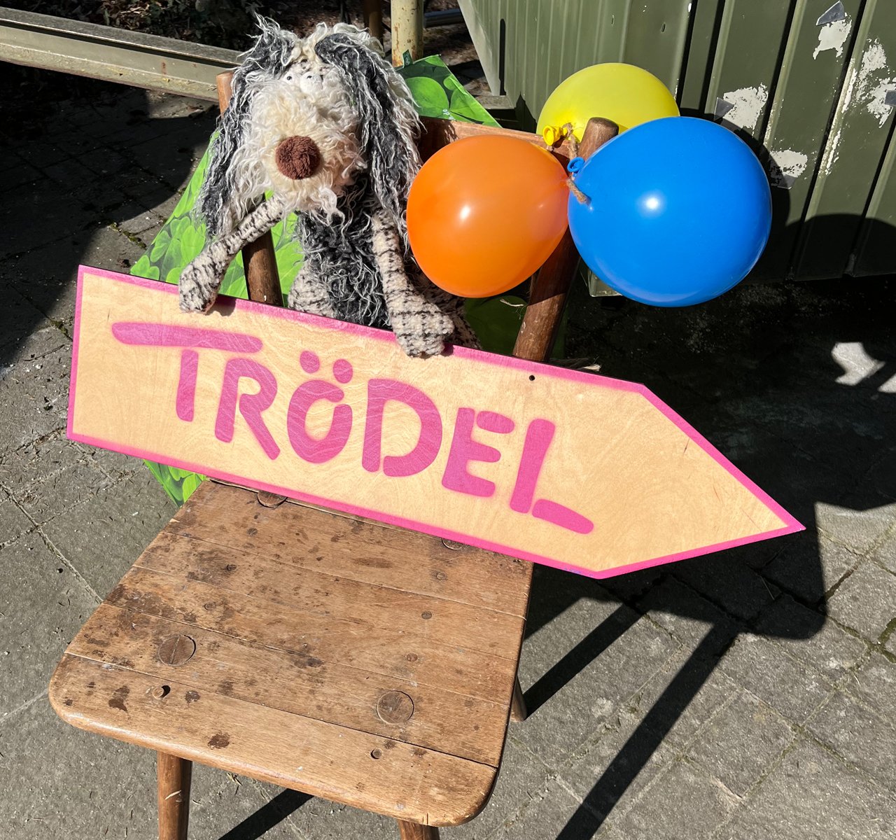 Holzstuhl mit Stoffhund und drei Luftballons hält ein Schild mit der Aufschrift 'TRÖDEL'