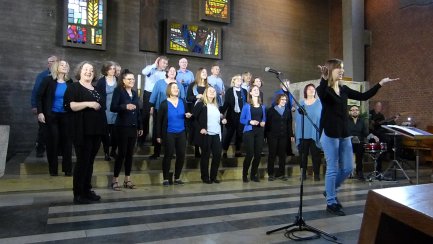 Der Chor auf einer Kirchenempore singt unter Leitung einer Dirigentin.