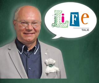 Martin Rassau in grauem Sakko und dunklem Hemd mit weißem Teddybär an der Brust vor grünem Hintergrund und Sprechblase mit buntem Schriftzug 'LIFE TALK'