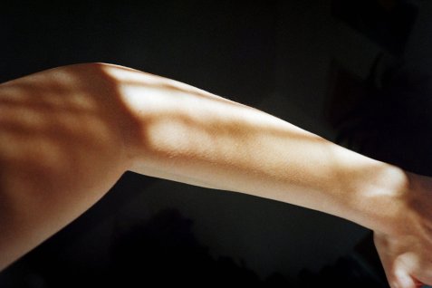 Bildausschnitt von einem Arm auf dem Sonnenlicht reflektiert vor dunklem Hintergrund.