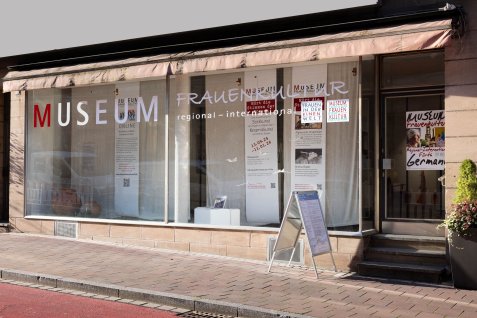 Schaufenster mit Schriftzug 'MUSEUM FRAUENMUSEUM regional - international' und mehreren Aushängen an der Fassade eines Museums