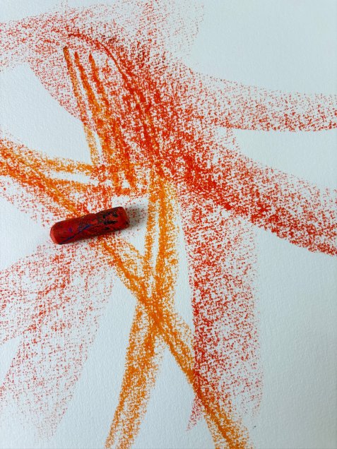 Roter Wachsmalstift auf Papier mit roten und orangen Farbspuren
