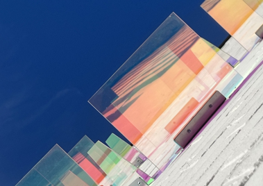 Mehrere transparente, farbige Glasplatten in unterschiedlicher Höhe auf einer weißen Treppe vor blauem Himmel
