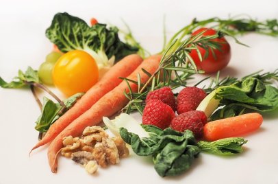 Nahaufnahme von Karotten, Himbeeren, Walnüssen, Spinatblättern, Tomaten und Trauben auf hellem Untergrund.
