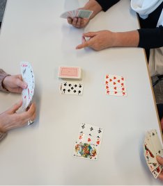 Foto von 4 Händen mit Spielkarten und einen Kartenstapel am Tisch