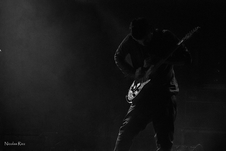 Silhouette einer Person, die auf einer dunklen, rauchigen Bühne im Gegenlicht E-Gitarre spielt.