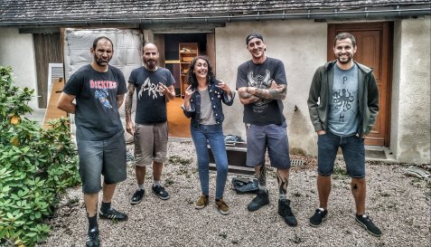 Fünf lachende Personen stehen in kurzen Hosen und T-Shirts vor einem Haus mit offener Garage im Hof.