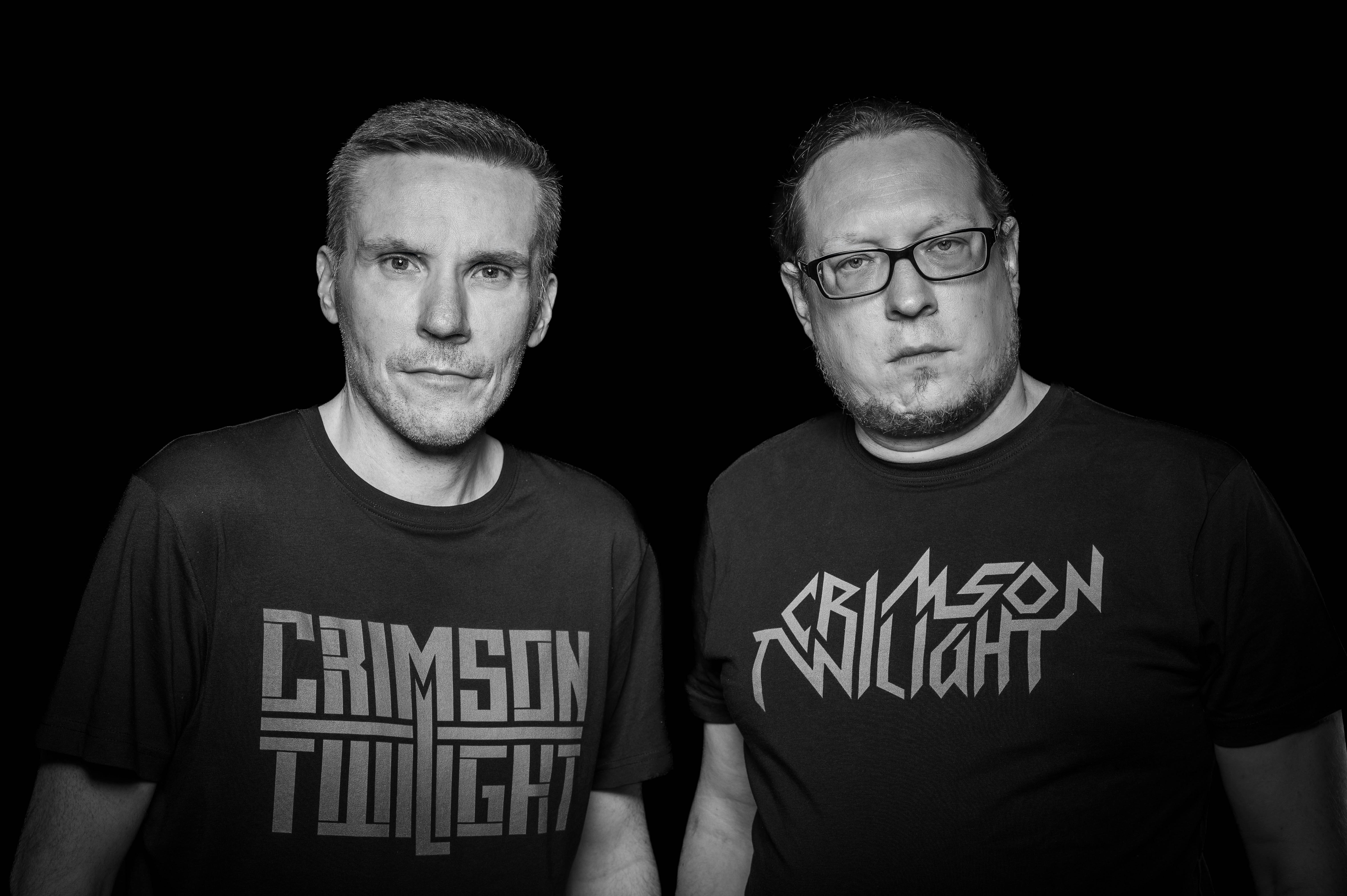 Schwarz-weißes Porträt von zwei Männern mit T-Shirts der Band „Crimson Twilight“ vor dunklem Hintergrund.