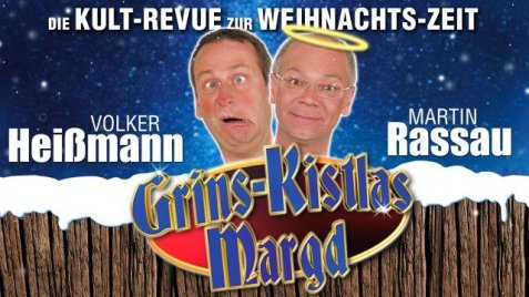 Heißmann & Rassau vor blauem Hintergrund, Rassau mit Heiligenschein, darunter der Schriftzug 'Grins-Kistlas Margd' auf Holzplanken,