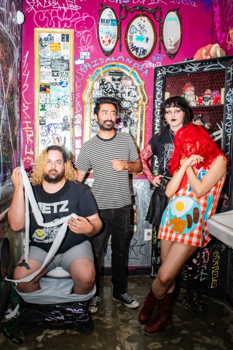 Vier Personen posieren humorvoll in einer mit Graffiti und Stickern bedeckten pinken Toilette.