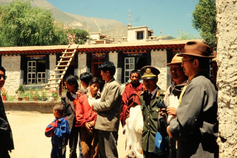 Gruppe von Menschen in traditioneller und moderner Kleidung 1994 in Osttibet vor einem Gebäude mit Holzleiter und Berg im Hintergrund