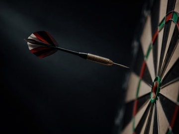 Ein Dartpfeil fliegt vor dunklem Hintergrund auf eine Dartscheibe zu.