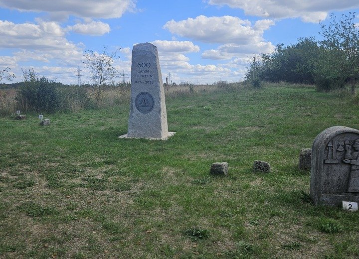 Ein Gedenkstein mit der Inschrift „600 Jahre Siebigerode“ steht auf einer Wiese, im Vordergrund ist eine weitere steinerne Gedenktafel zu sehen.