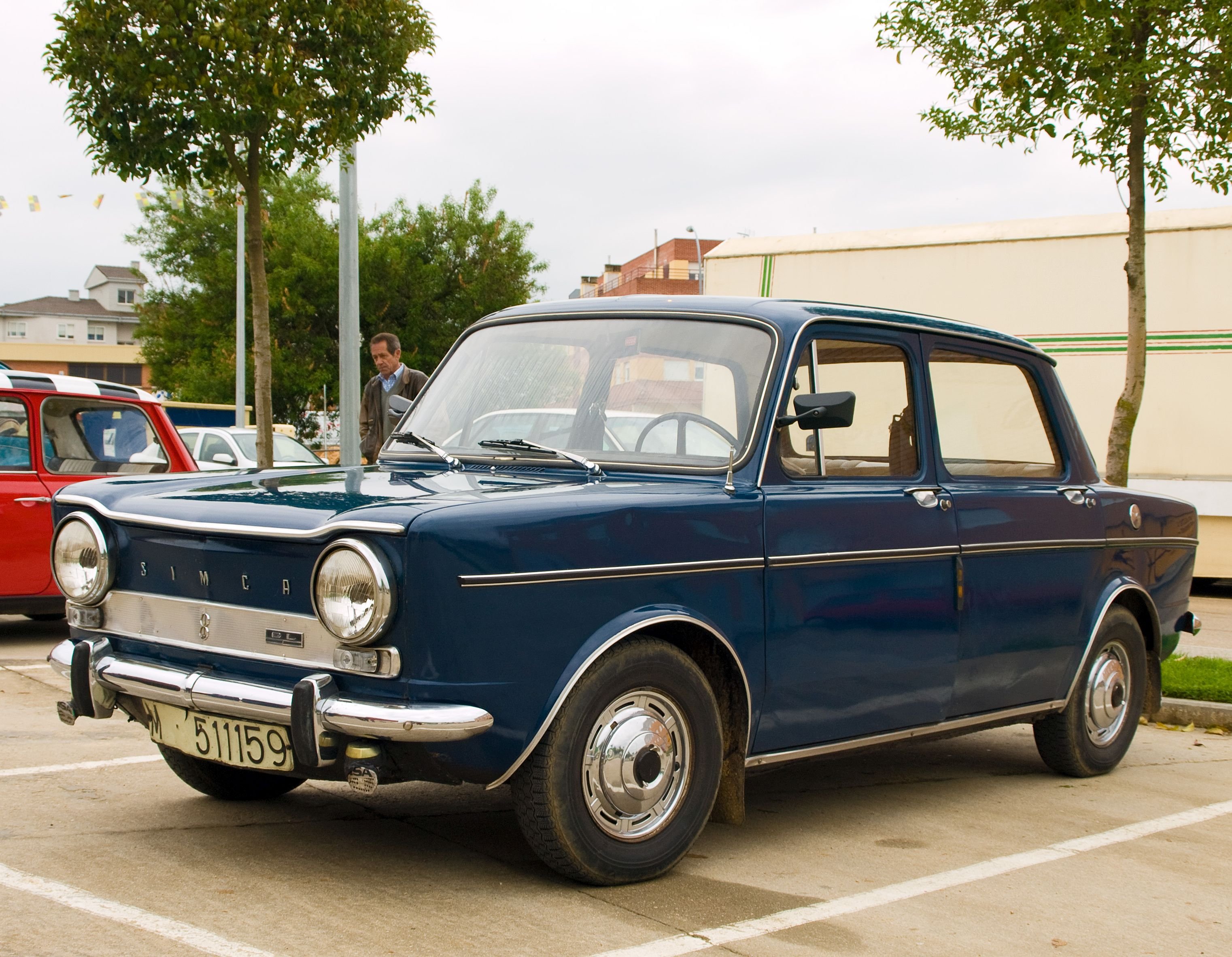 Ein dunkelblauer Simca 1000 GL steht auf einem Parkplatz, im Hintergrund sind Bäume und weitere Oldtimer zu sehen.